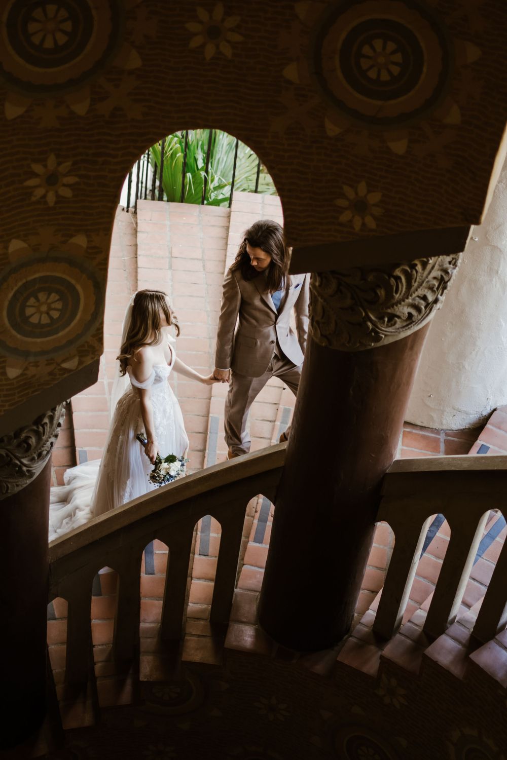 A serene moment in a quiet stairwell captures two figures standing in an arched doorway on a sunny day.