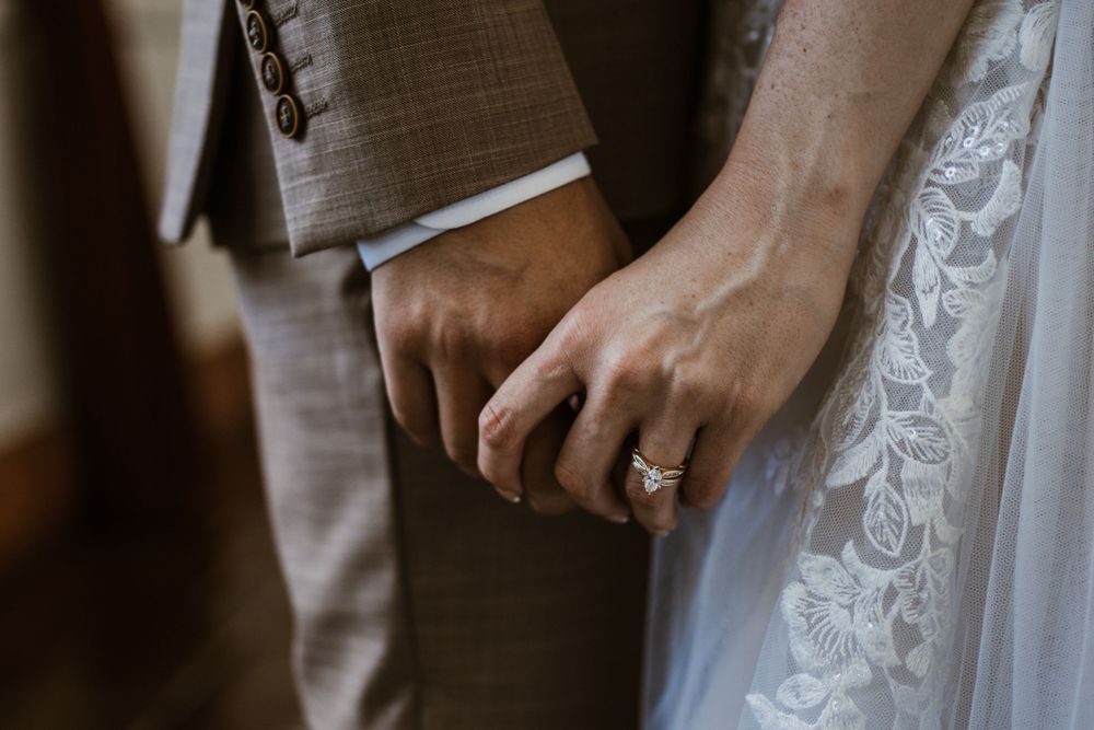 Close up of newlywed couple holding hands showing wedding rings and lace dress details.