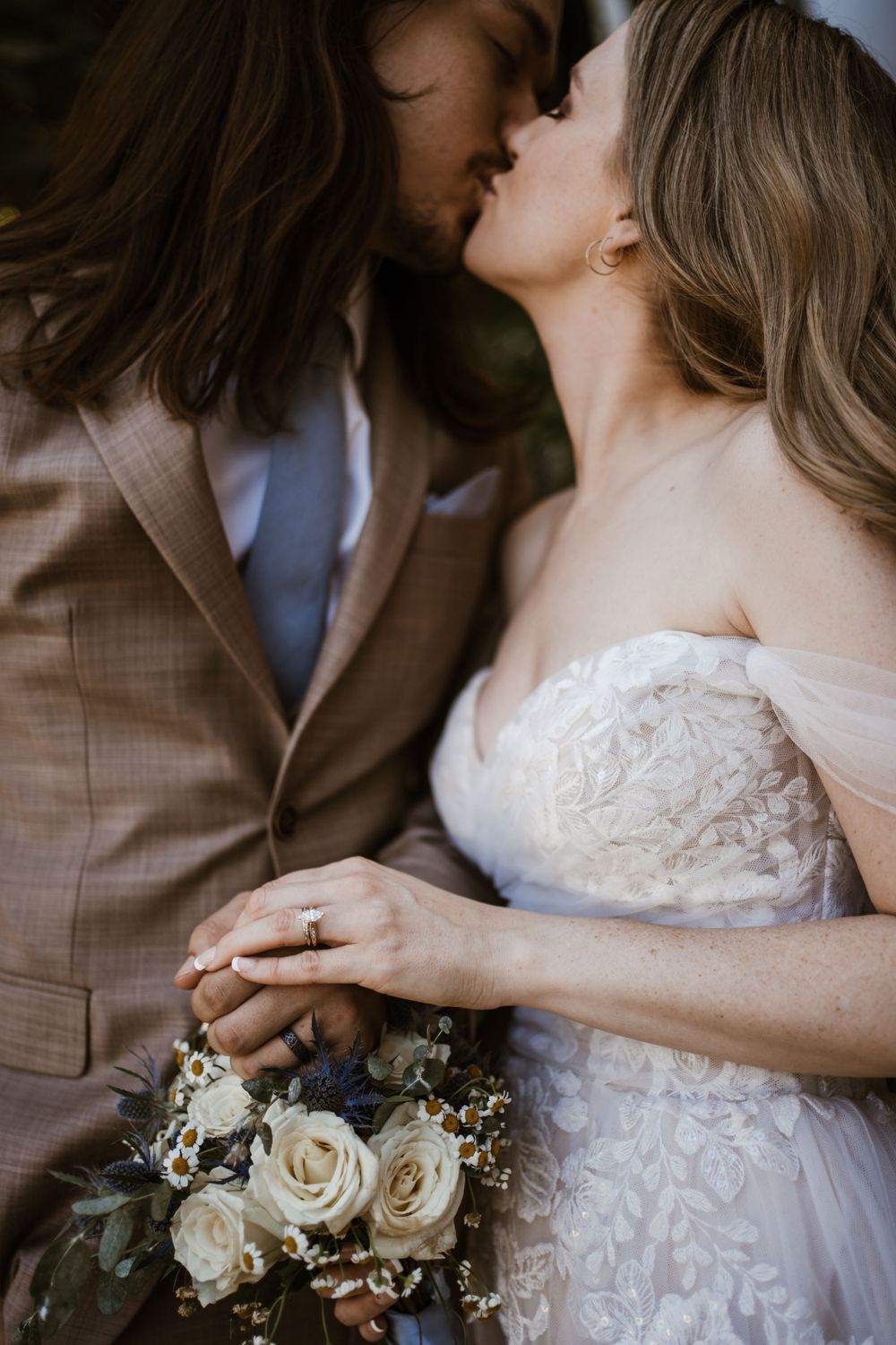 A romantic wedding moment captured with white roses bouquet as couple shares an intimate kiss outdoors.