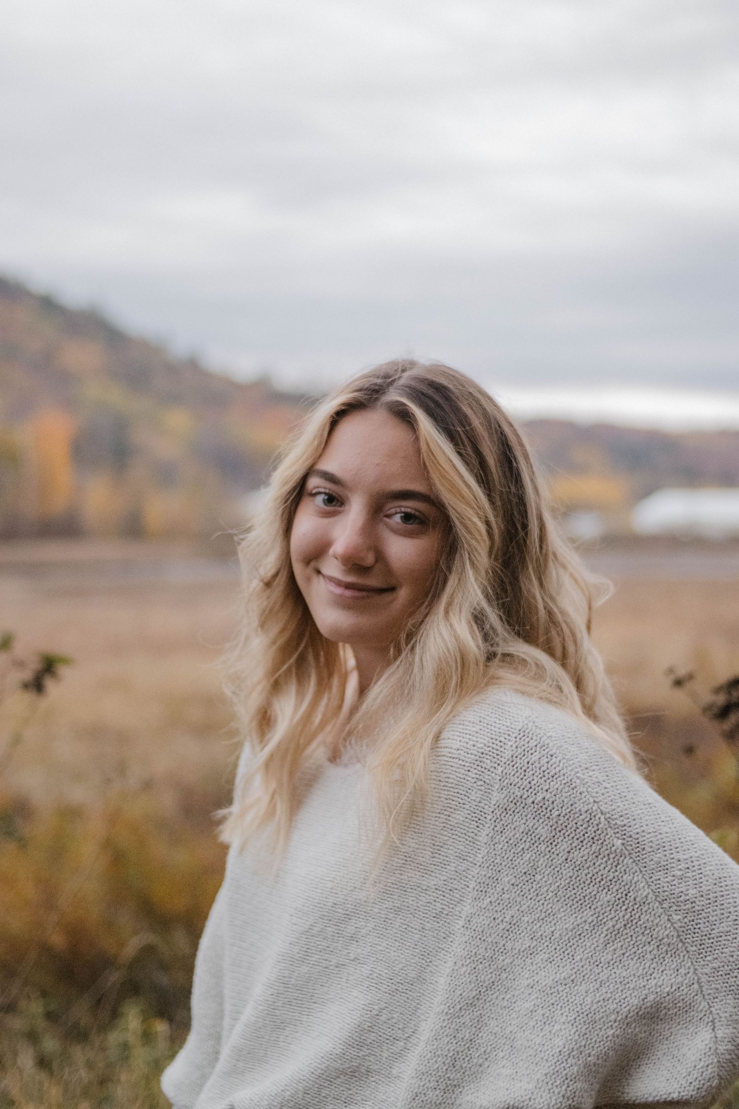 Person in white sweater enjoying a cloudy autumn day in nature.