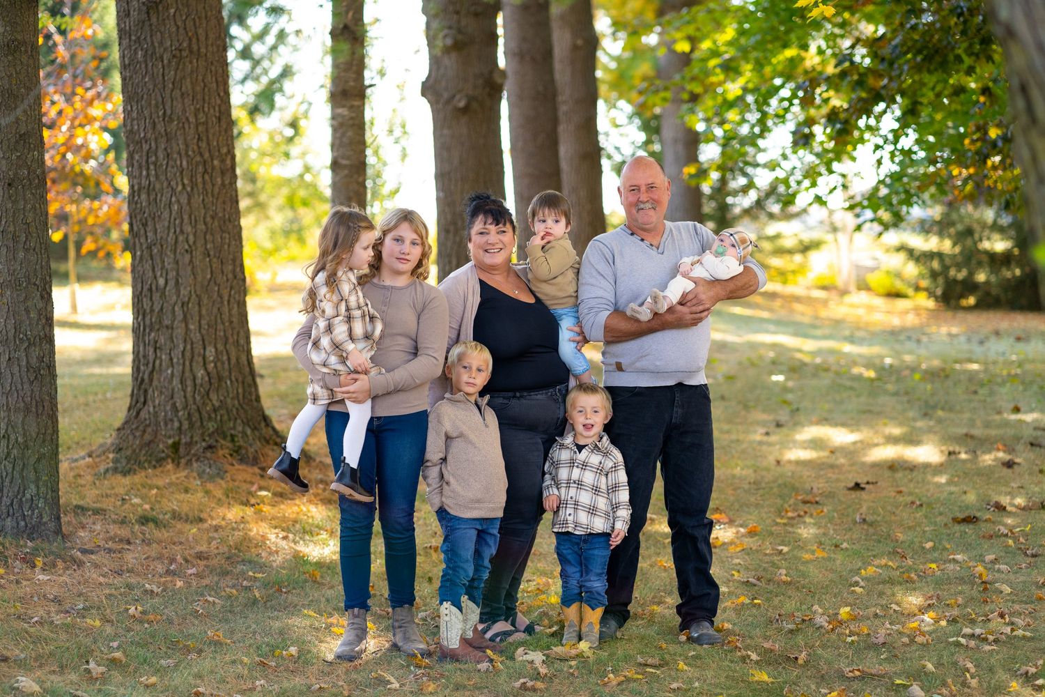 Family group poses together under tall trees during autumn photo session.