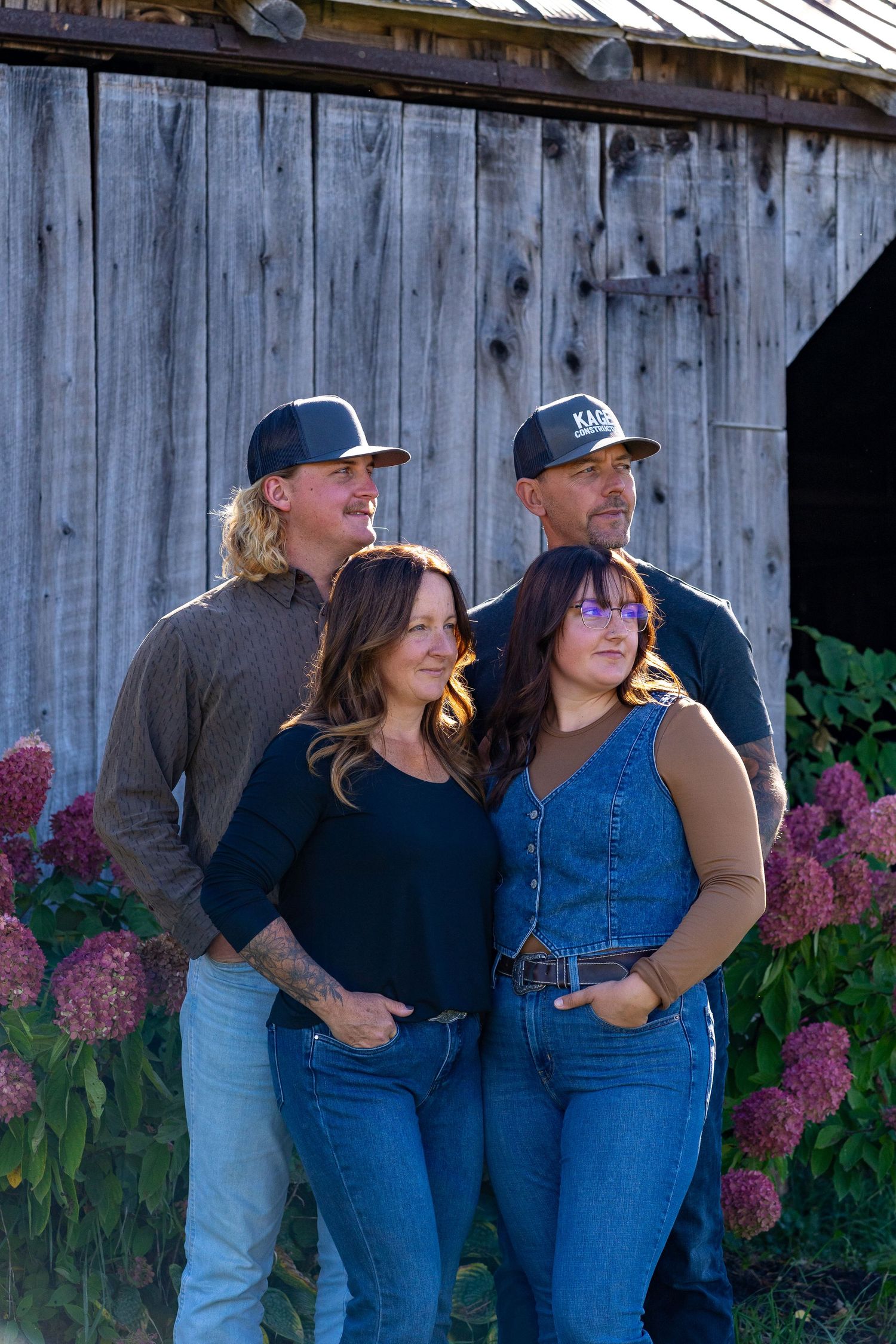 Group portrait in casual wear standing against a rustic barn with blooming hydrangeas.