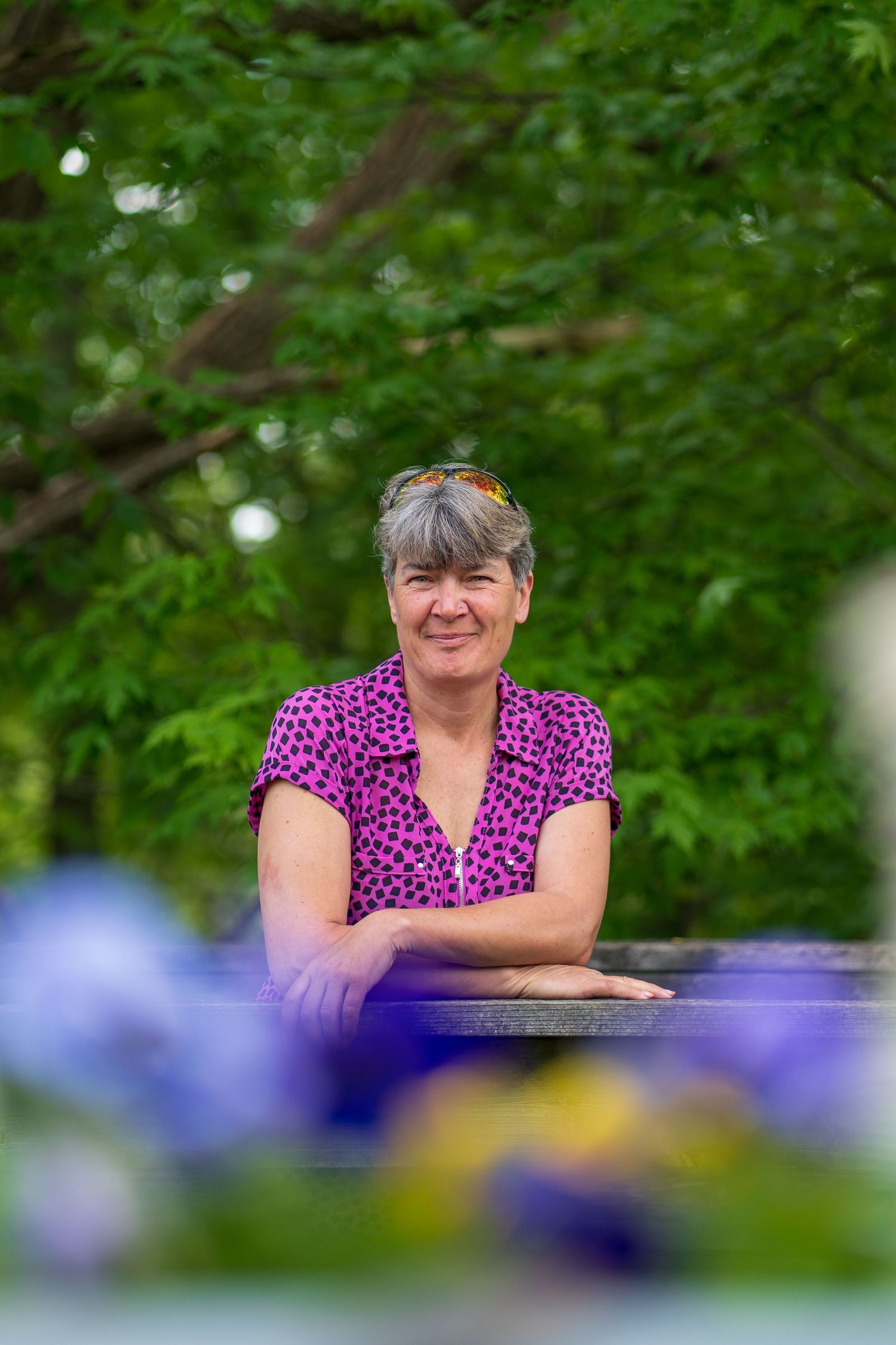 A person in a purple polka dot shirt sits at an outdoor table with flowers in the foreground.