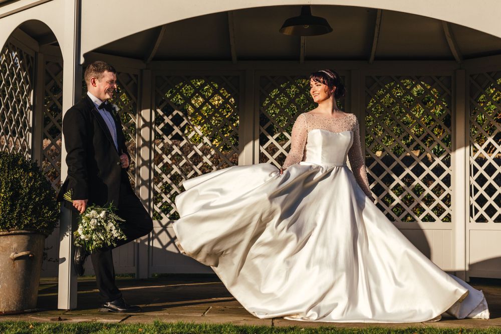 A dramatic wedding portrait showing a flowing white dress in an elegant garden gazebo setting.