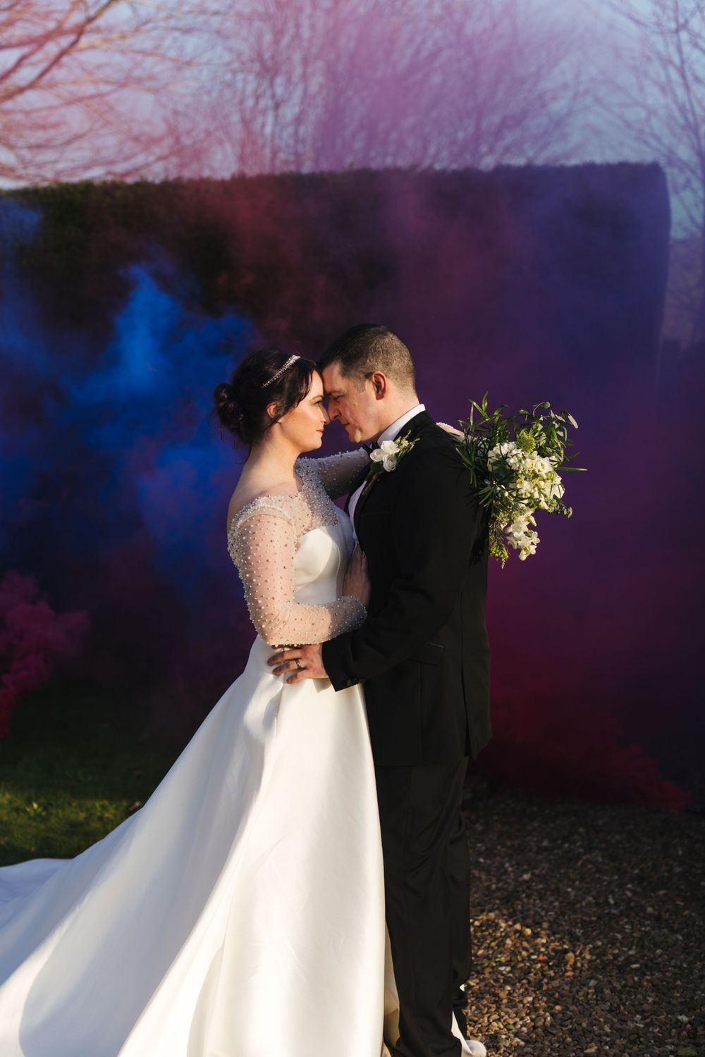 Intimate wedding photo with blue and purple smoke effects showcasing an elegant white gown and bouquet.