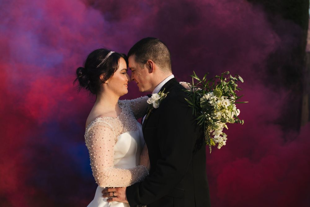 Artistic wedding photo captured against a vivid red and blue smoke backdrop.