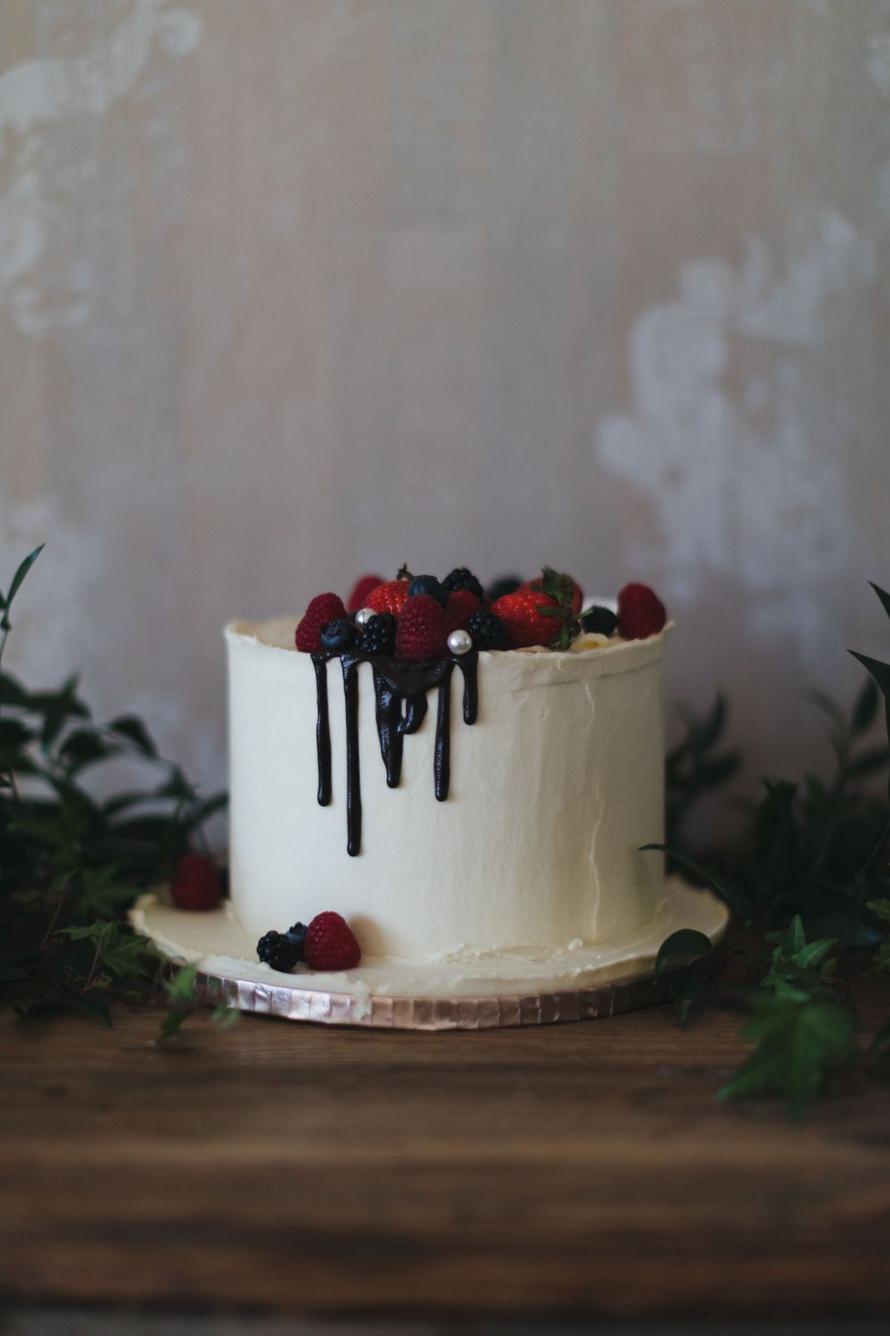 Minimalist white wedding cake adorned with dark chocolate drips and fresh mixed berries.