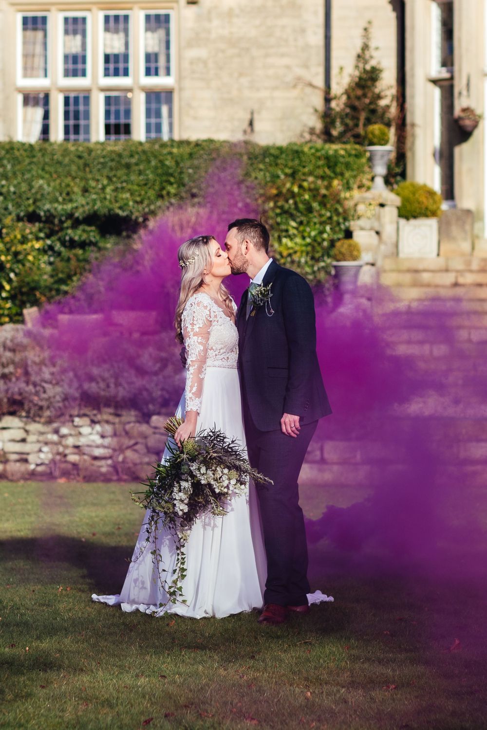Wedding portrait with purple smoke bomb effect in front of a stone building.