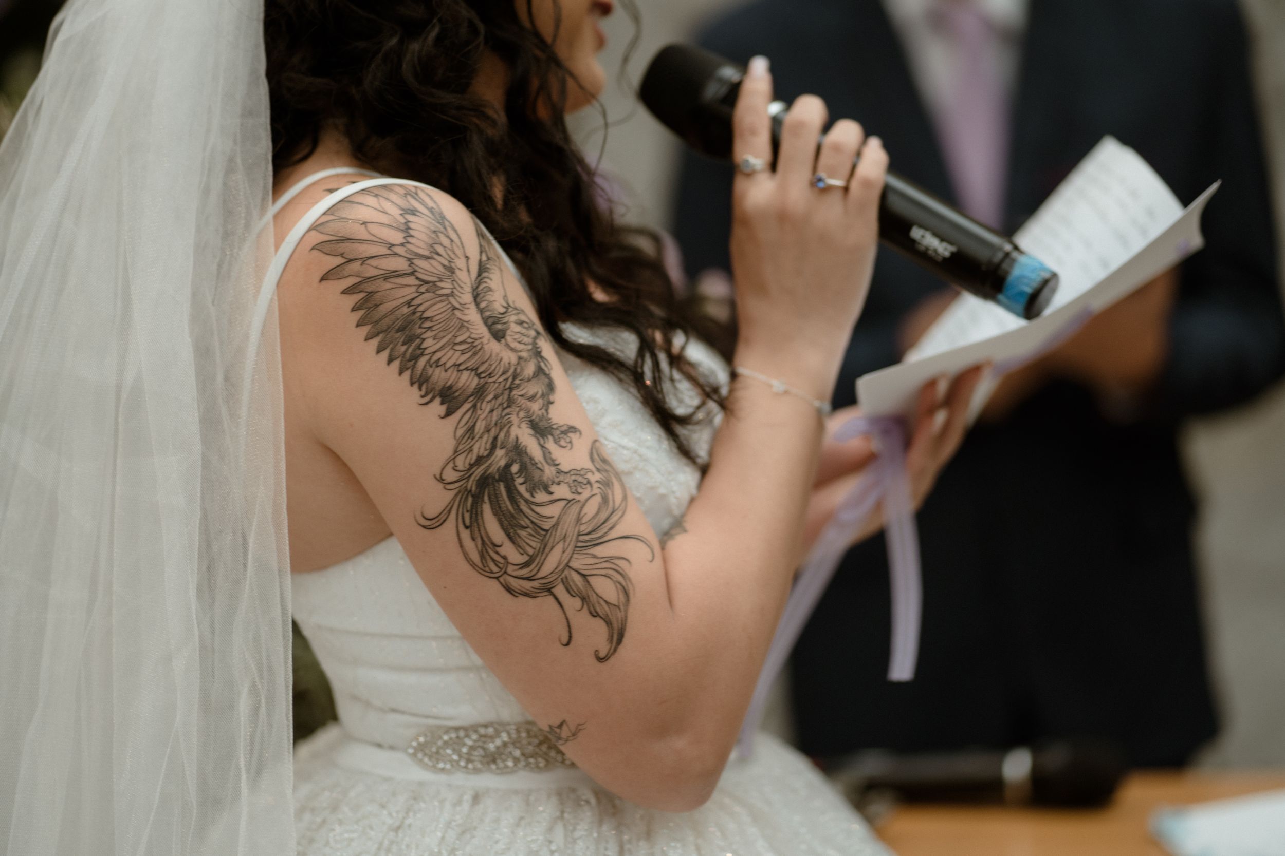 Wedding ceremony with tattooed bride in white dress holding microphone.