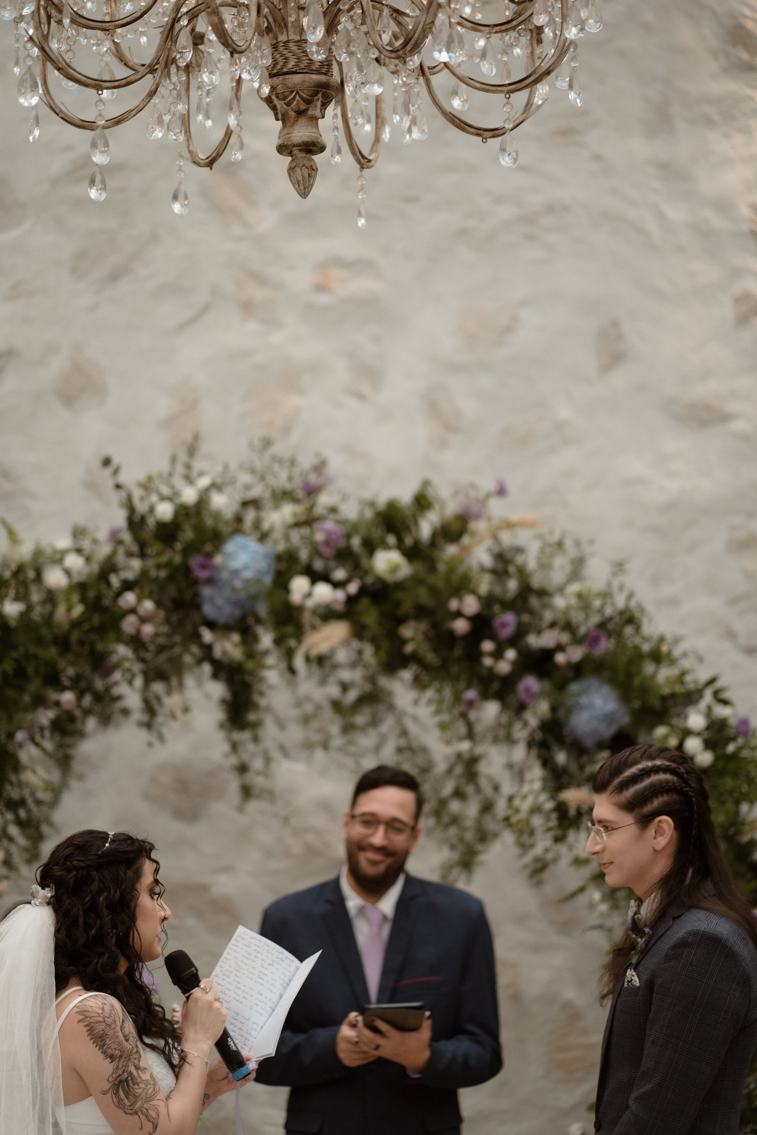 Wedding ceremony under crystal chandeliers with greenery arch decoration.