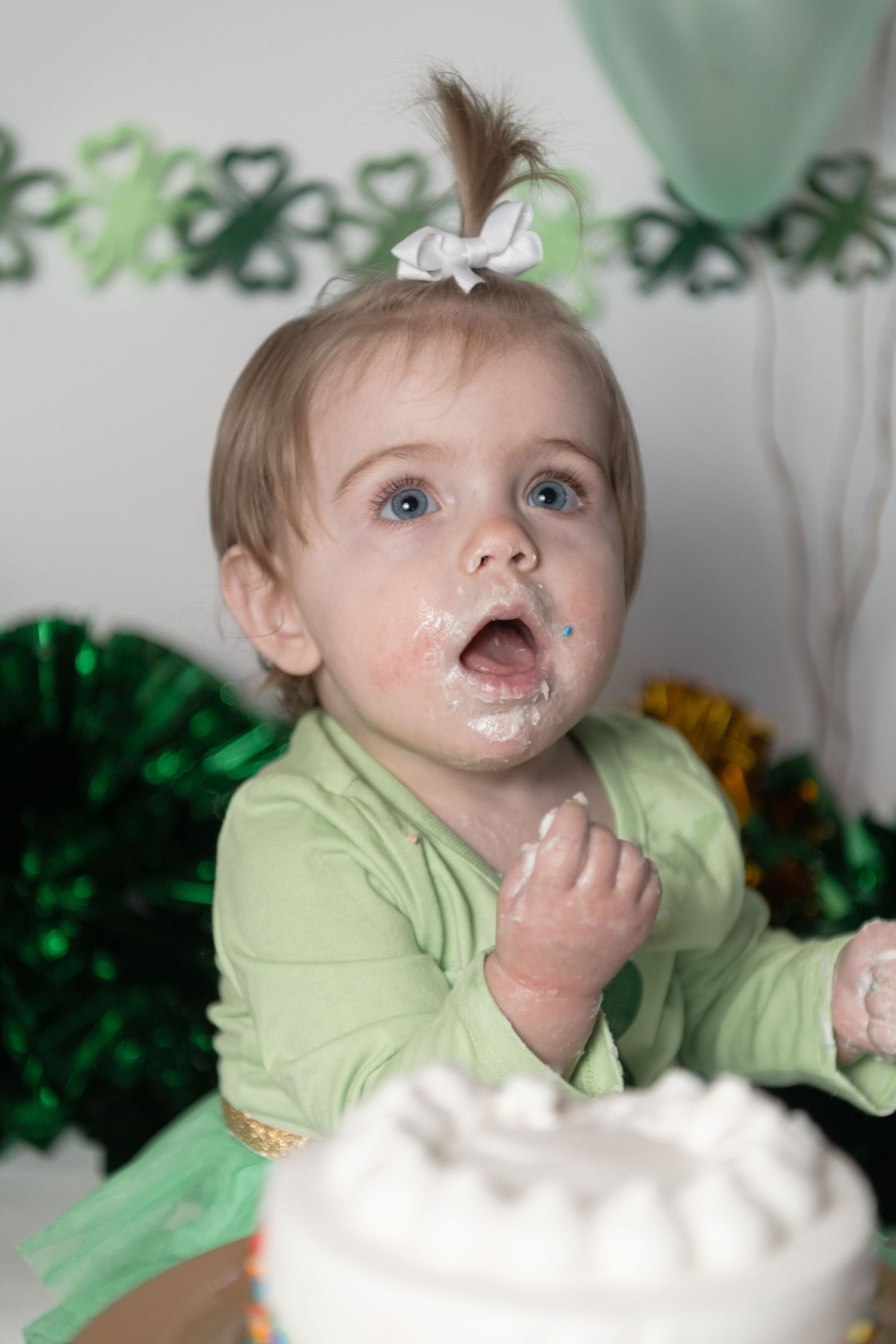 Toddler in green dress enjoying cake during St. Patrick's Day celebration.