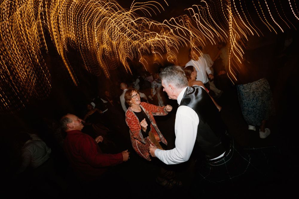 Guests dancing energetically at a wedding reception under dramatic string light decorations.