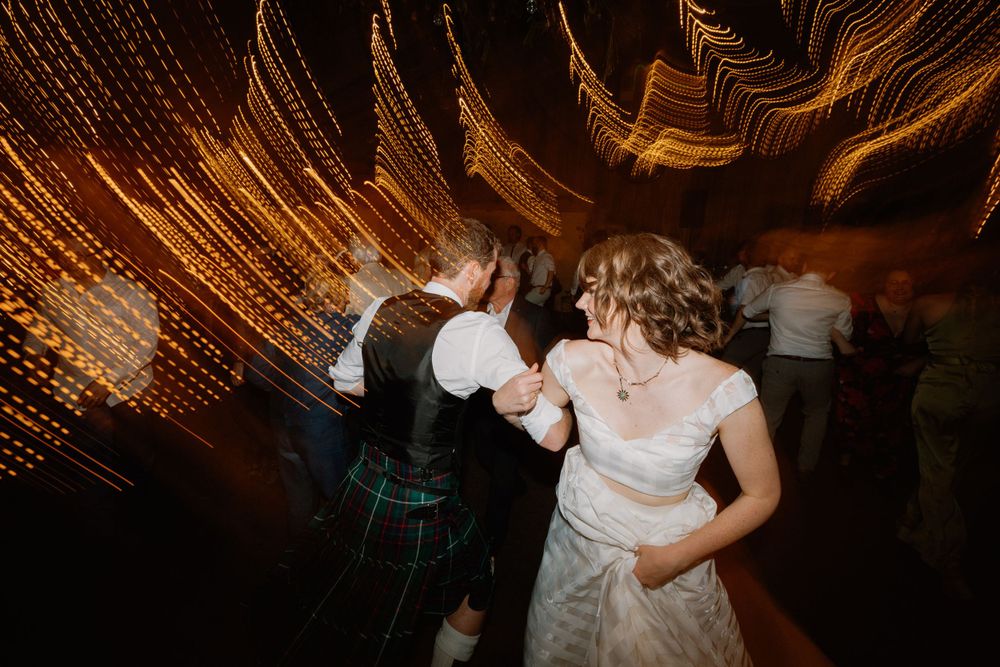 Dancing figures create motion blur beneath warm fairy lights at an evening celebration.