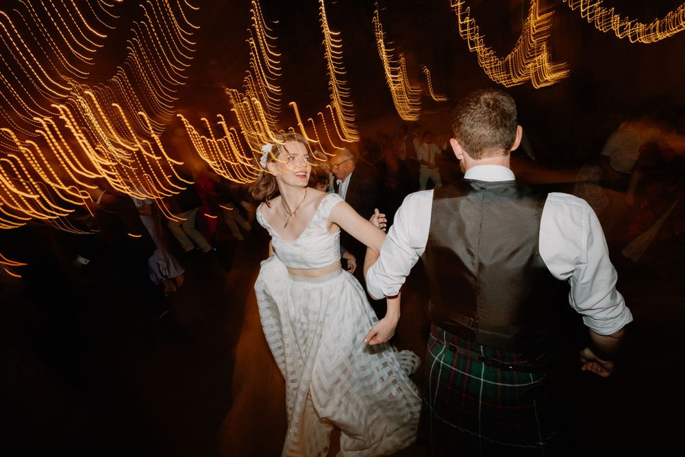 A couple dances under glowing string lights at a wedding reception with dramatic motion blur effects.