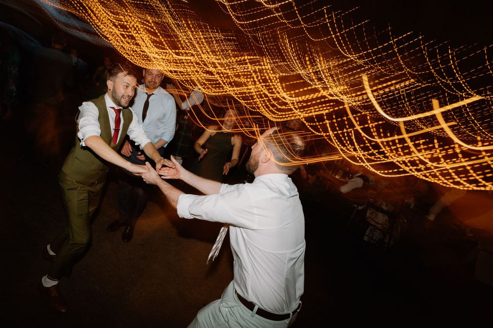 Dynamic dance moves captured at a wedding reception under glowing string lights.