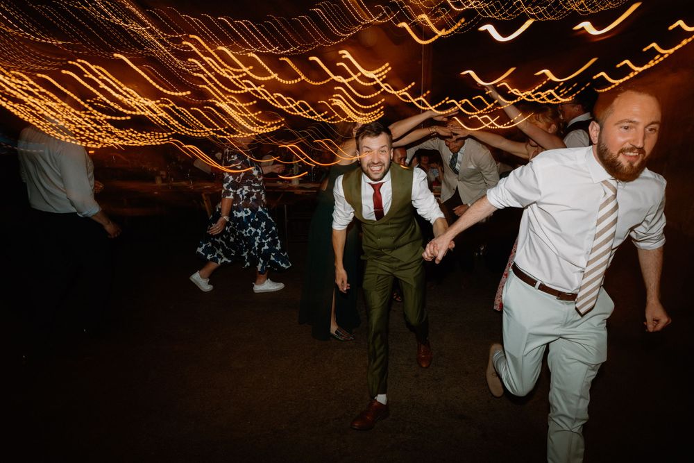 Wedding guests dancing with enthusiasm under string lights at an indoor venue.