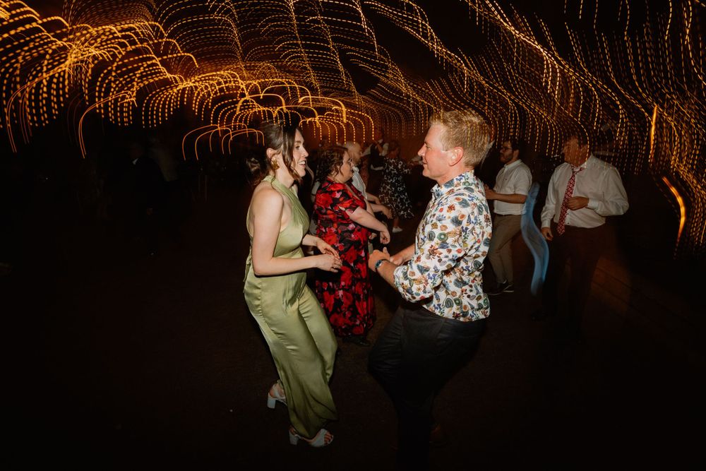 Energetic dancing at a wedding reception under warm string light patterns.