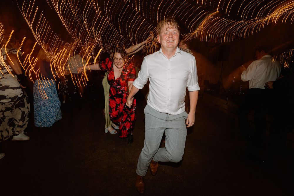 People dancing enthusiastically under warm fairy lights at a wedding reception.