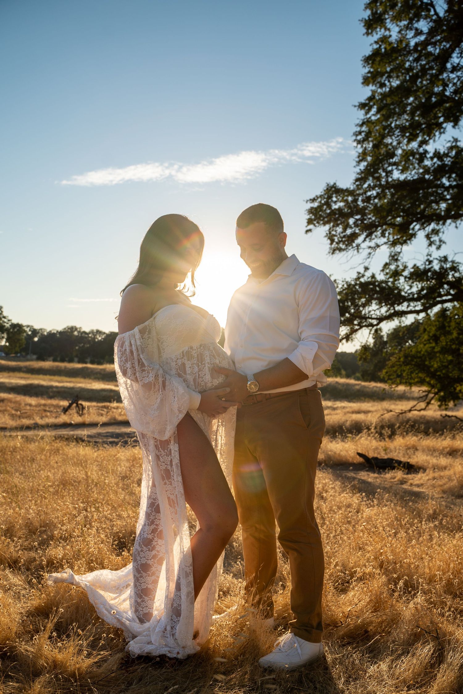 Couple shares intimate moment in golden field during maternity photoshoot.