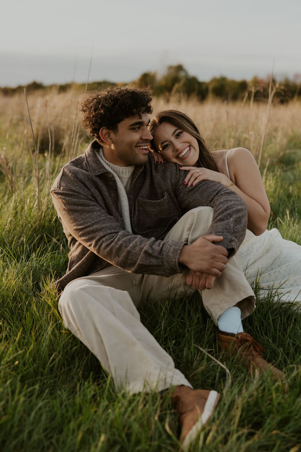 A couple lies together in tall grass during a romantic outdoor photoshoot at golden hour.
