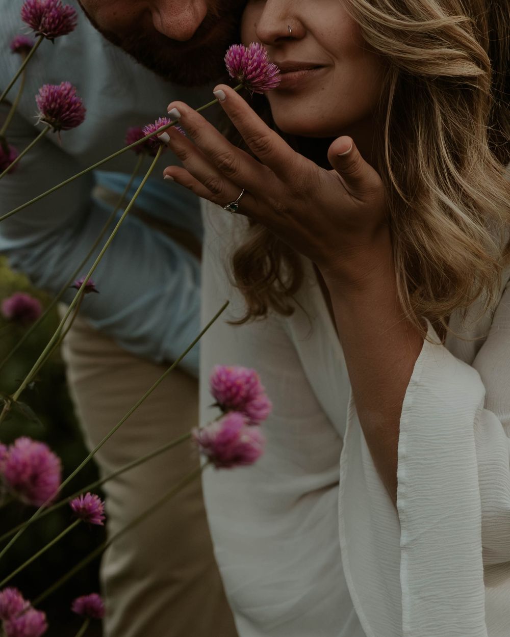Person in white top admiring pink clover flowers growing in garden during summer.