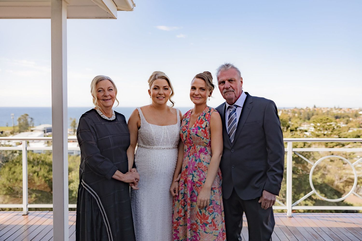 A group poses together on a sunny balcony with coastal views in the background.