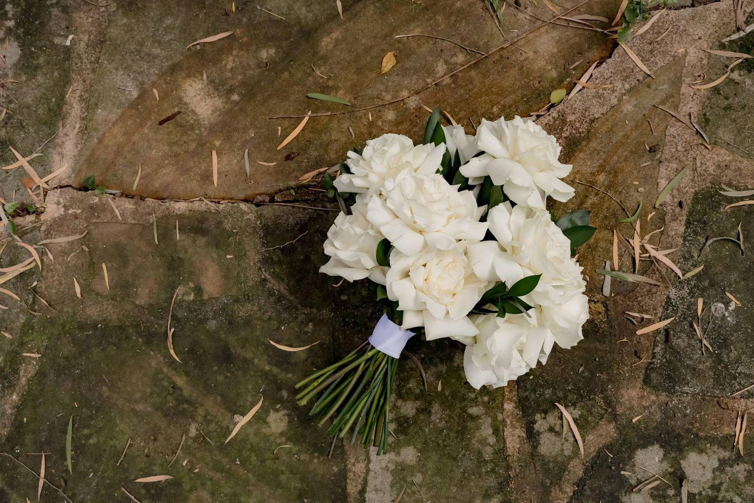 A classic white carnation wedding bouquet rests on a rustic textured surface.