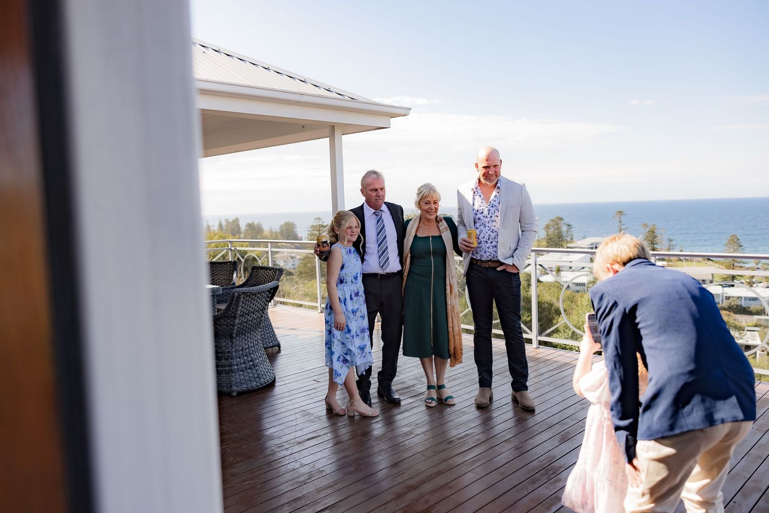 Wedding guests gather on a coastal deck with ocean views in the background.