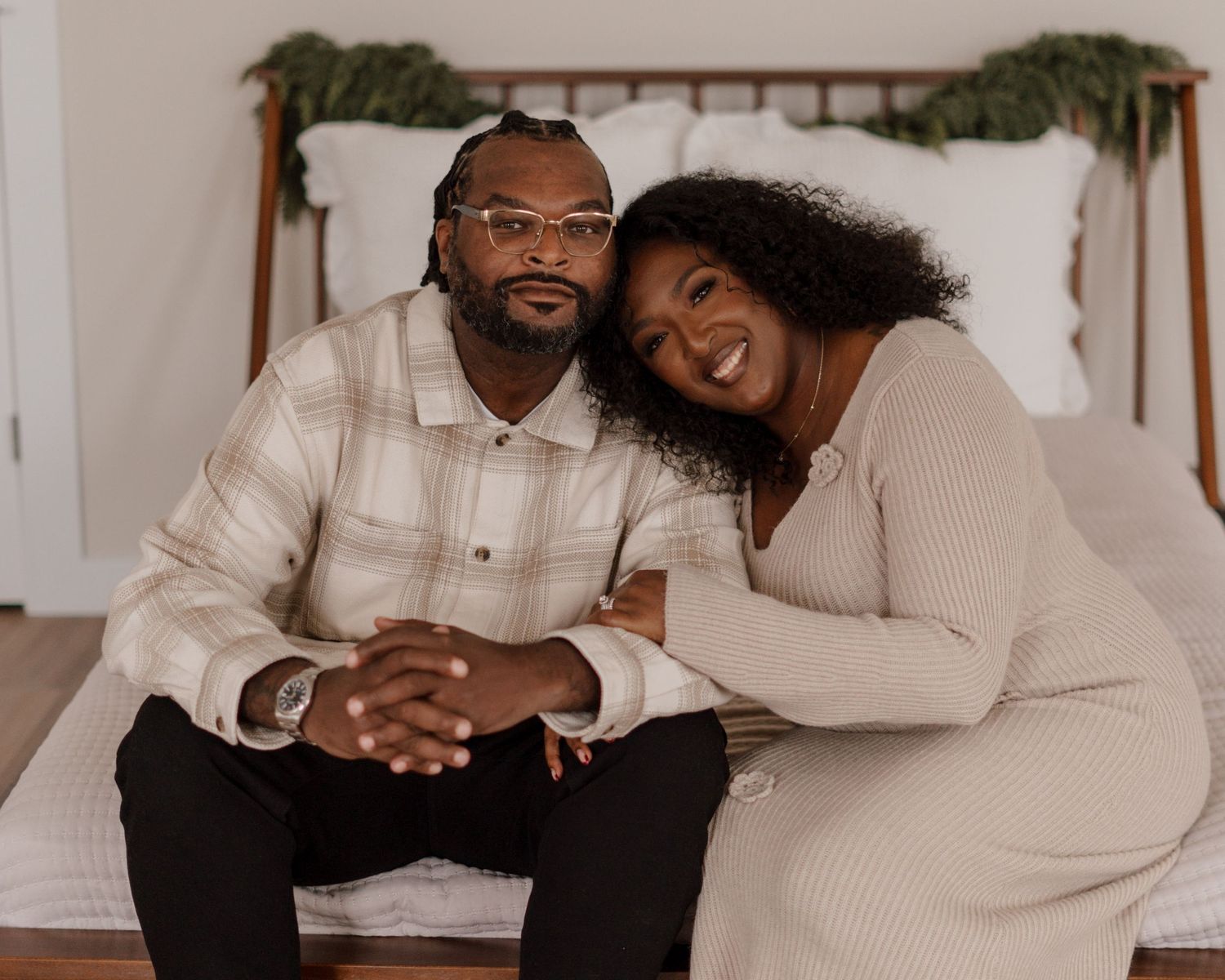 Cozy indoor portrait of couple sitting on bench with holiday greenery decoration.