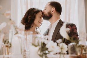 Romantic couple shares an intimate moment during their wedding ceremony in a softly lit venue with white floral decor.