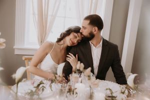 Romantic couple sharing intimate moments at an elegant wedding reception table with white floral centerpieces.