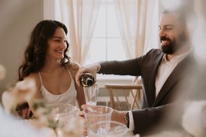 A couple shares a romantic moment while pouring wine at an intimate indoor dining setting.