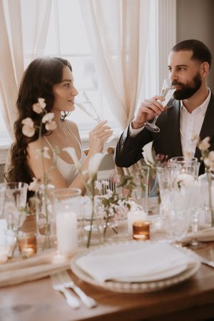 A couple sits at an elegant wedding reception table with white floral centerpieces and glowing candles.