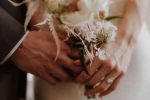 Close-up details of hands holding delicate white flowers and floral arrangements against a neutral background.