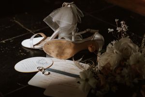 Wedding accessories including white shoes and delicate floral arrangements displayed on dark background.