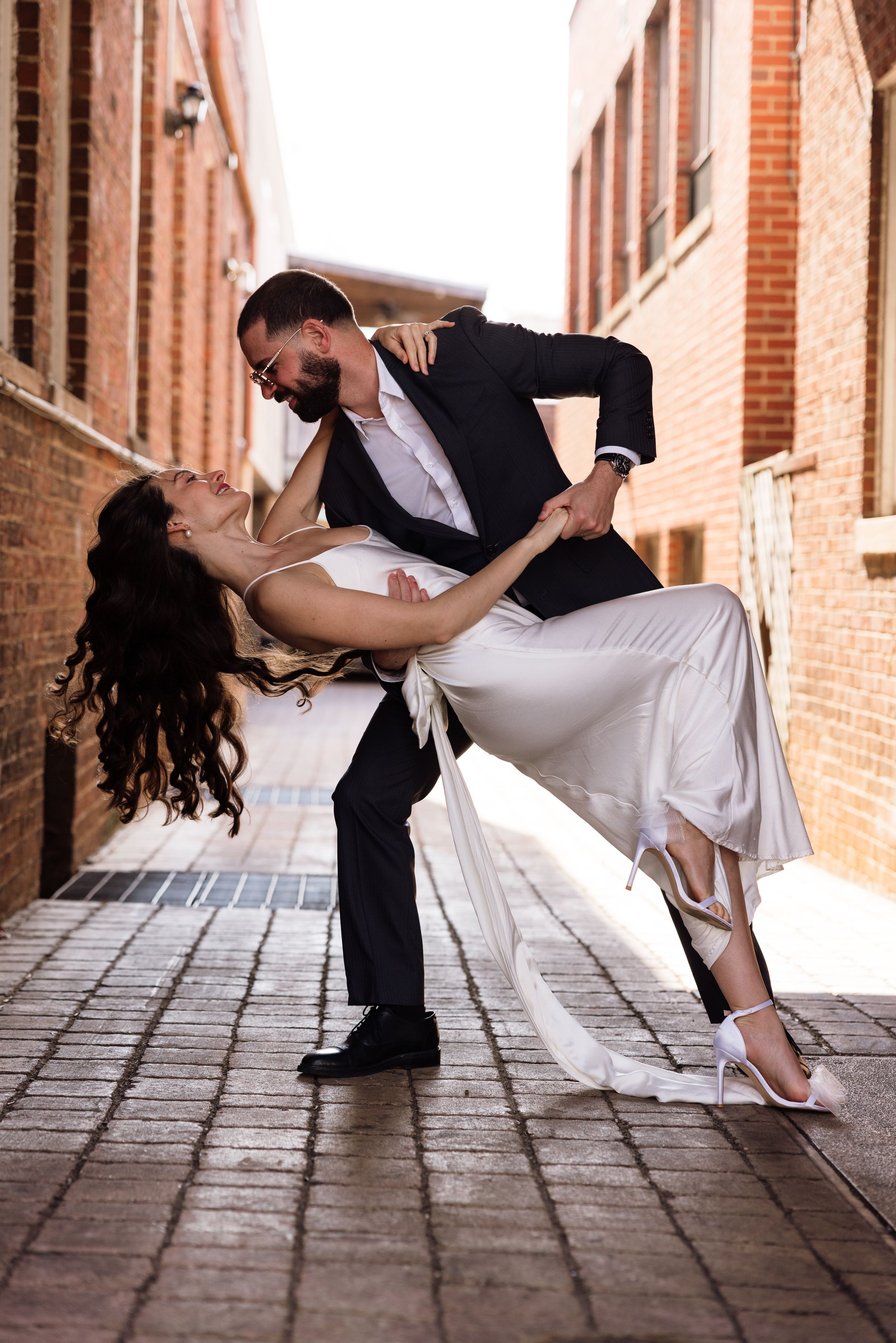 Romantic dance dip sequence showing couple in wedding attire against brick building exterior.