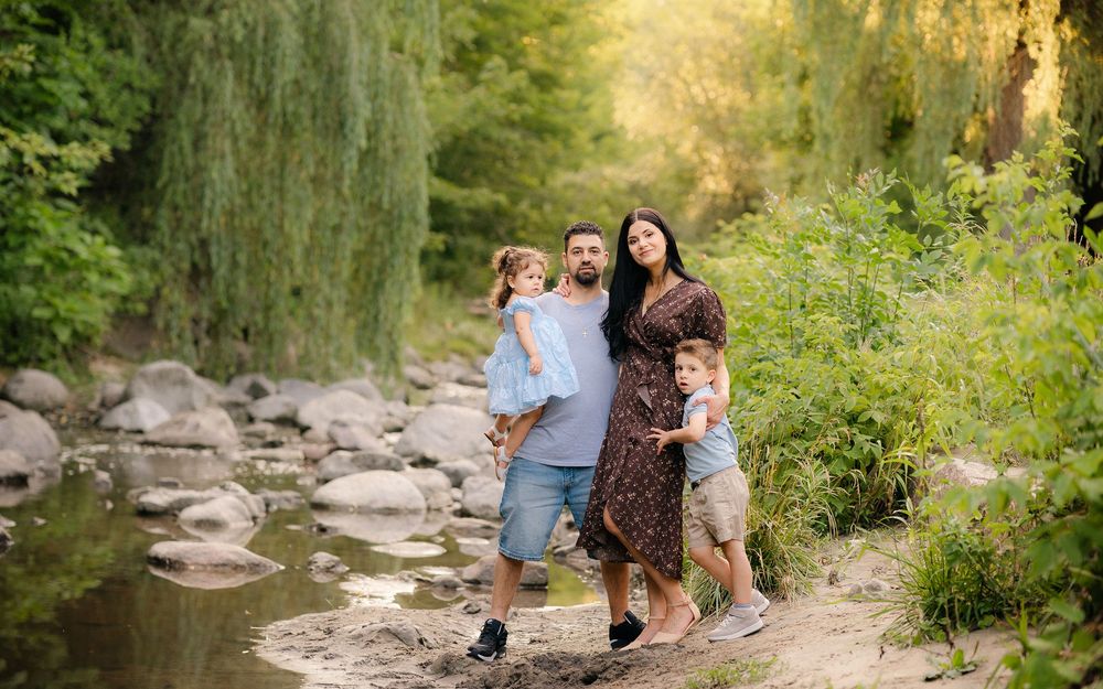 Family enjoying nature together on a rocky stream bank in a lush green forest setting during golden hour.