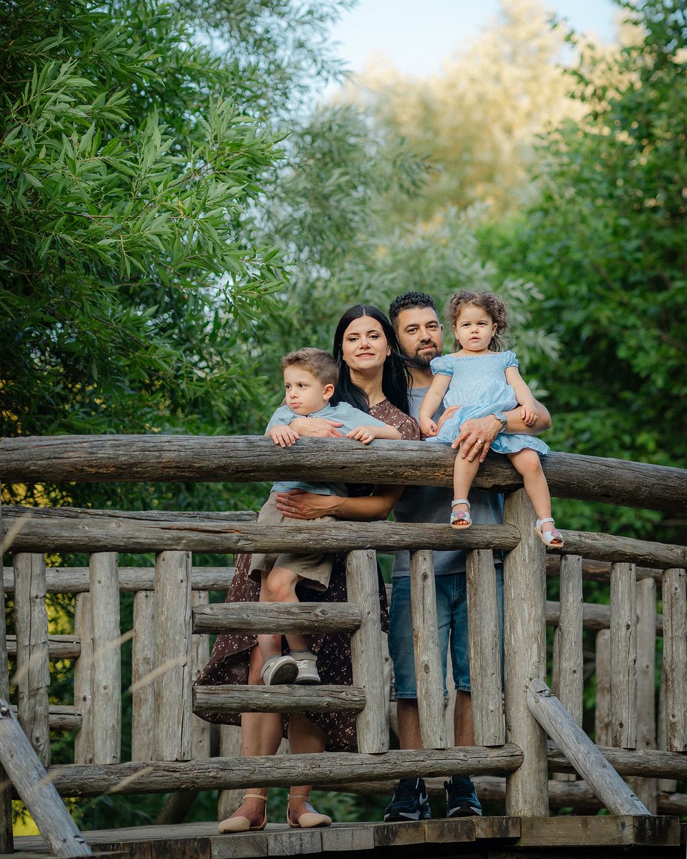 People sitting together on a rustic wooden bridge railing in a peaceful outdoor setting amidst greenery.