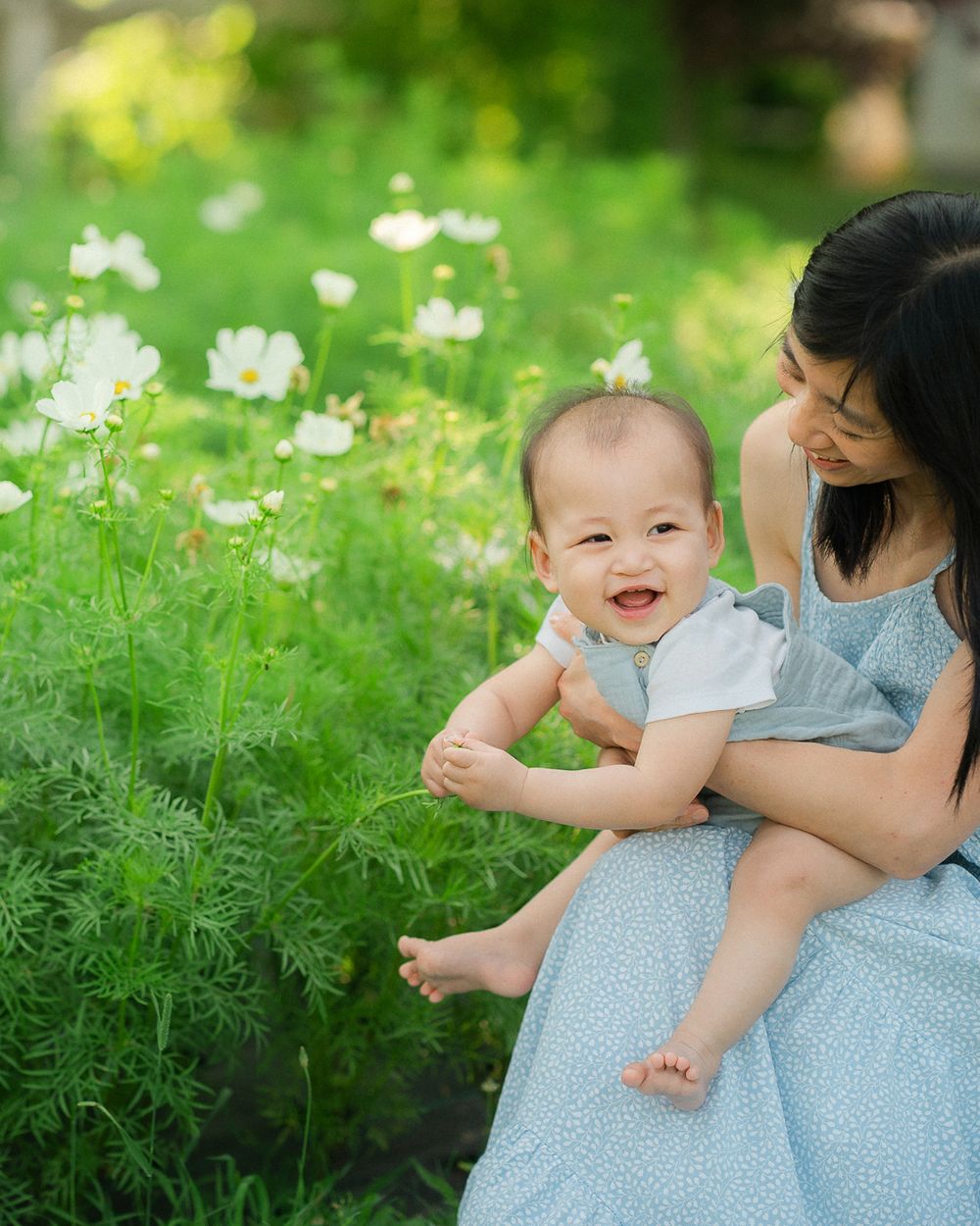 Parent and child share tender moments together while sitting in a blooming flower field on a sunny day.