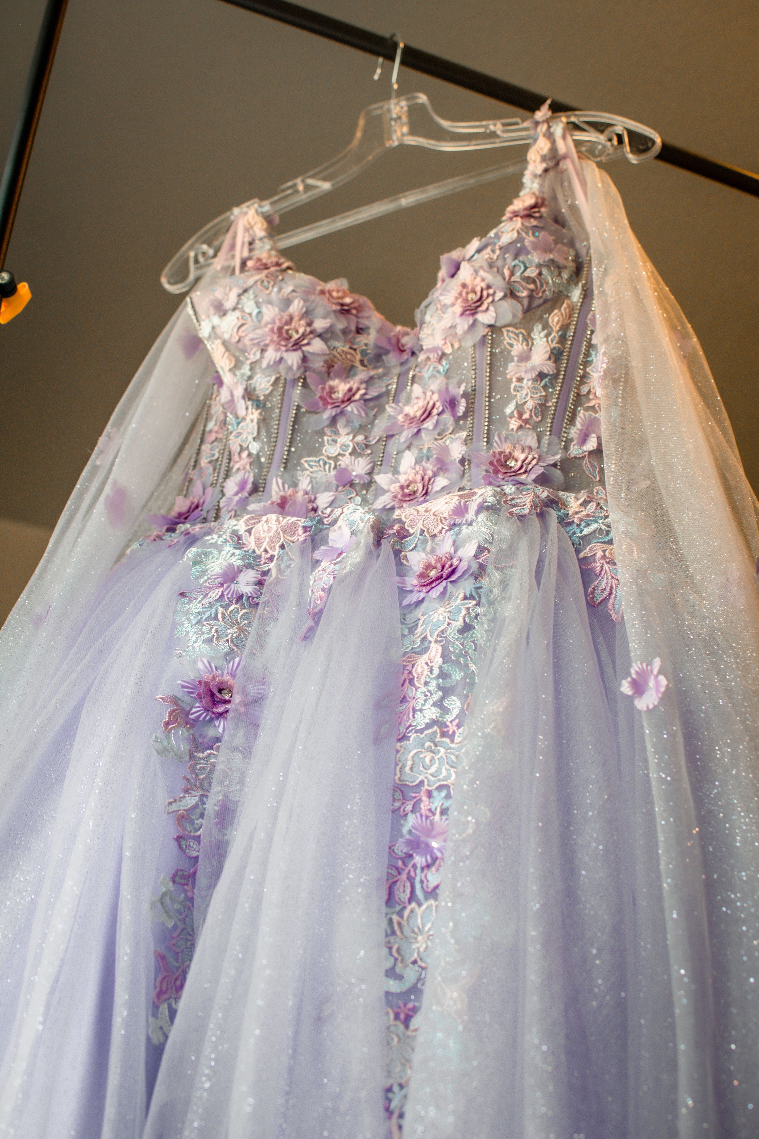 Lavender princess ball gown with floral details hanging on display.
