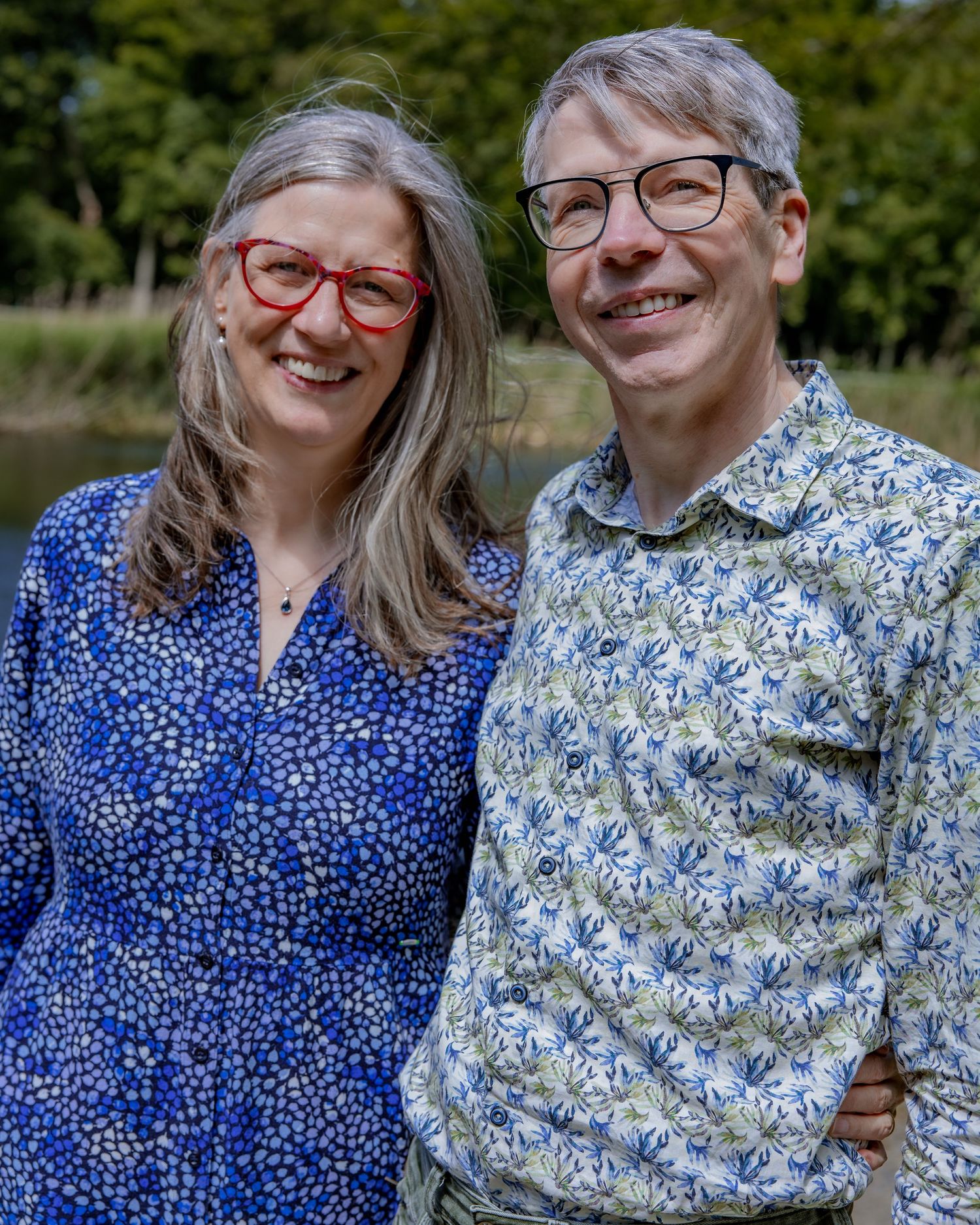 A happy couple wearing matching patterned shirts smile together in an outdoor garden setting.

- BU Photography -