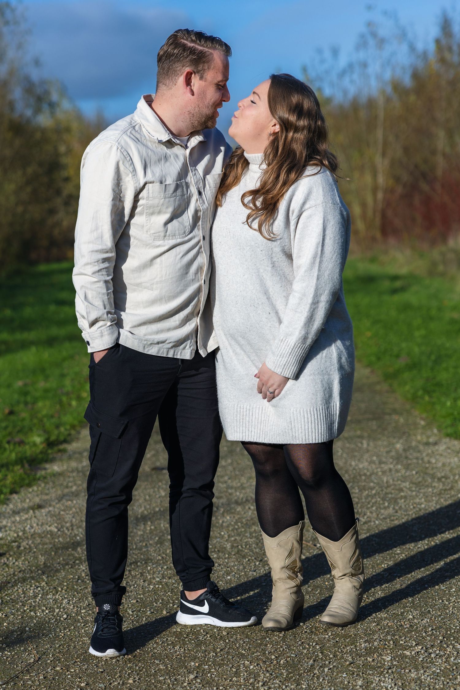 Two people sharing a romantic moment on a path outdoors wearing casual winter clothing and boots on an autumn day.