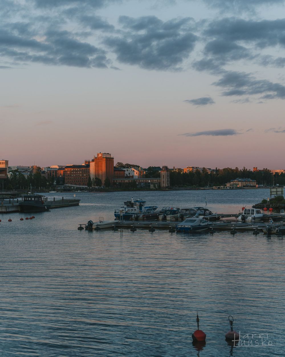 Waterfront cityscape at sunset with boats docked at the marina.