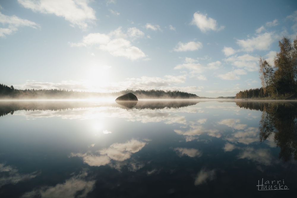 Misty morning lake landscape with perfect cloud reflections and sunlight breaking through.