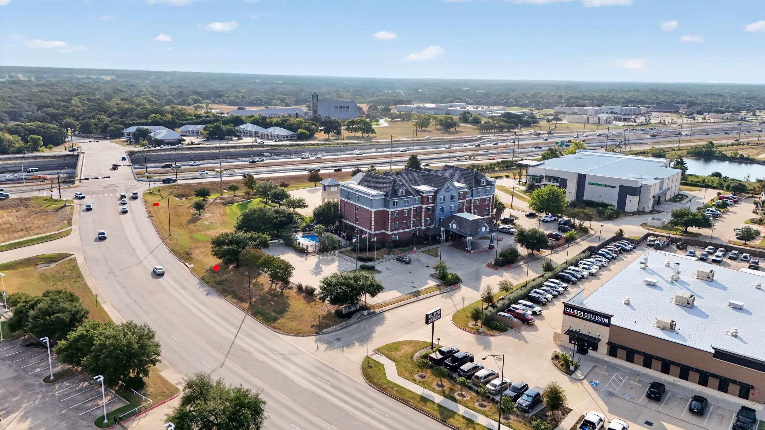 Aerial view of a brick commercial building near a highway intersection surrounded by parking lots and trees in a suburban area.