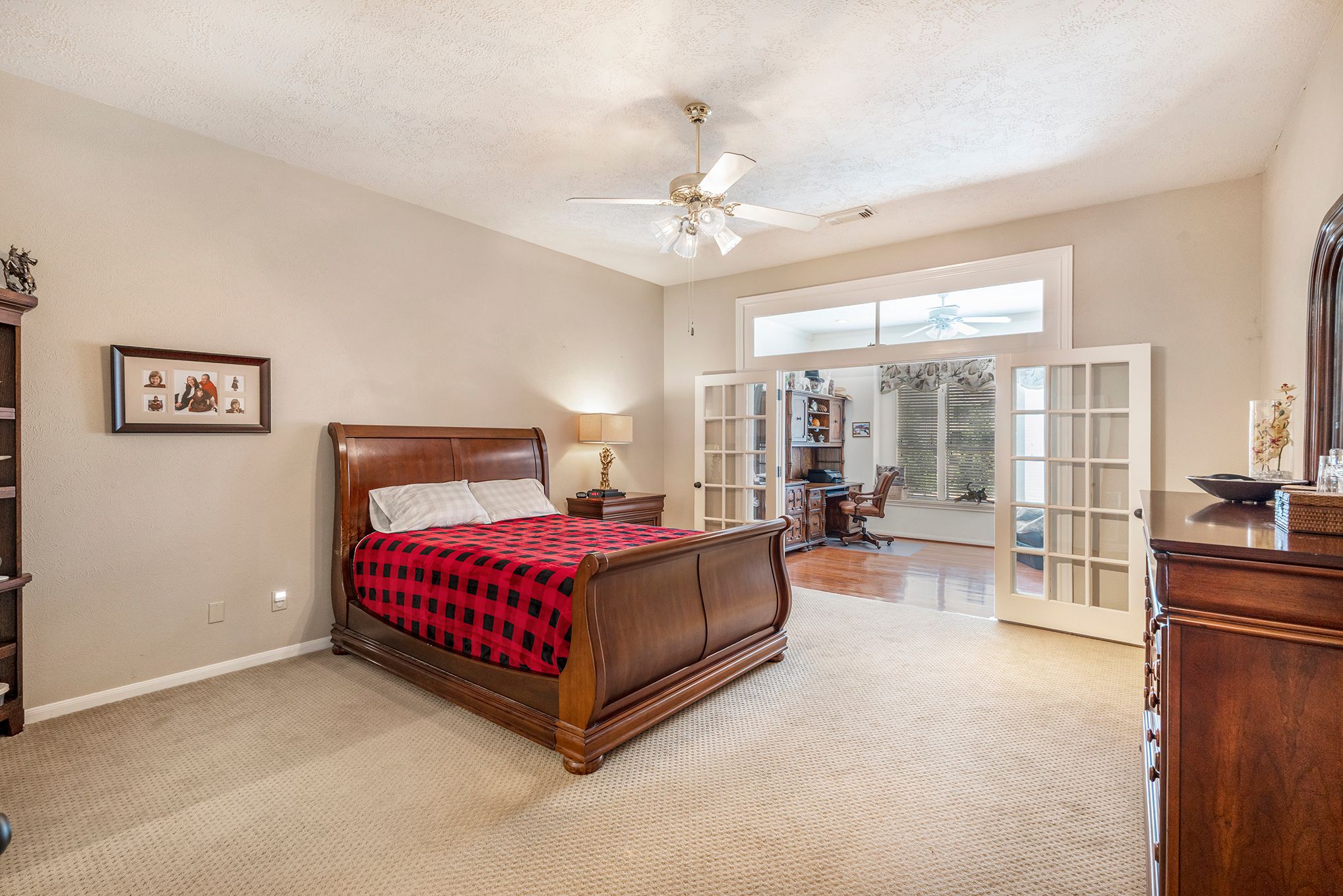 Spacious master bedroom with wood sleigh bed, red plaid bedding, French doors, and ceiling fan in neutral tones.