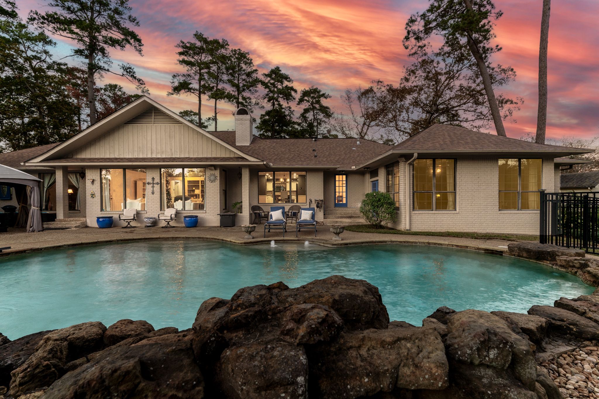 Luxury swimming pool with rock features and glowing lights against a vibrant sunset sky.