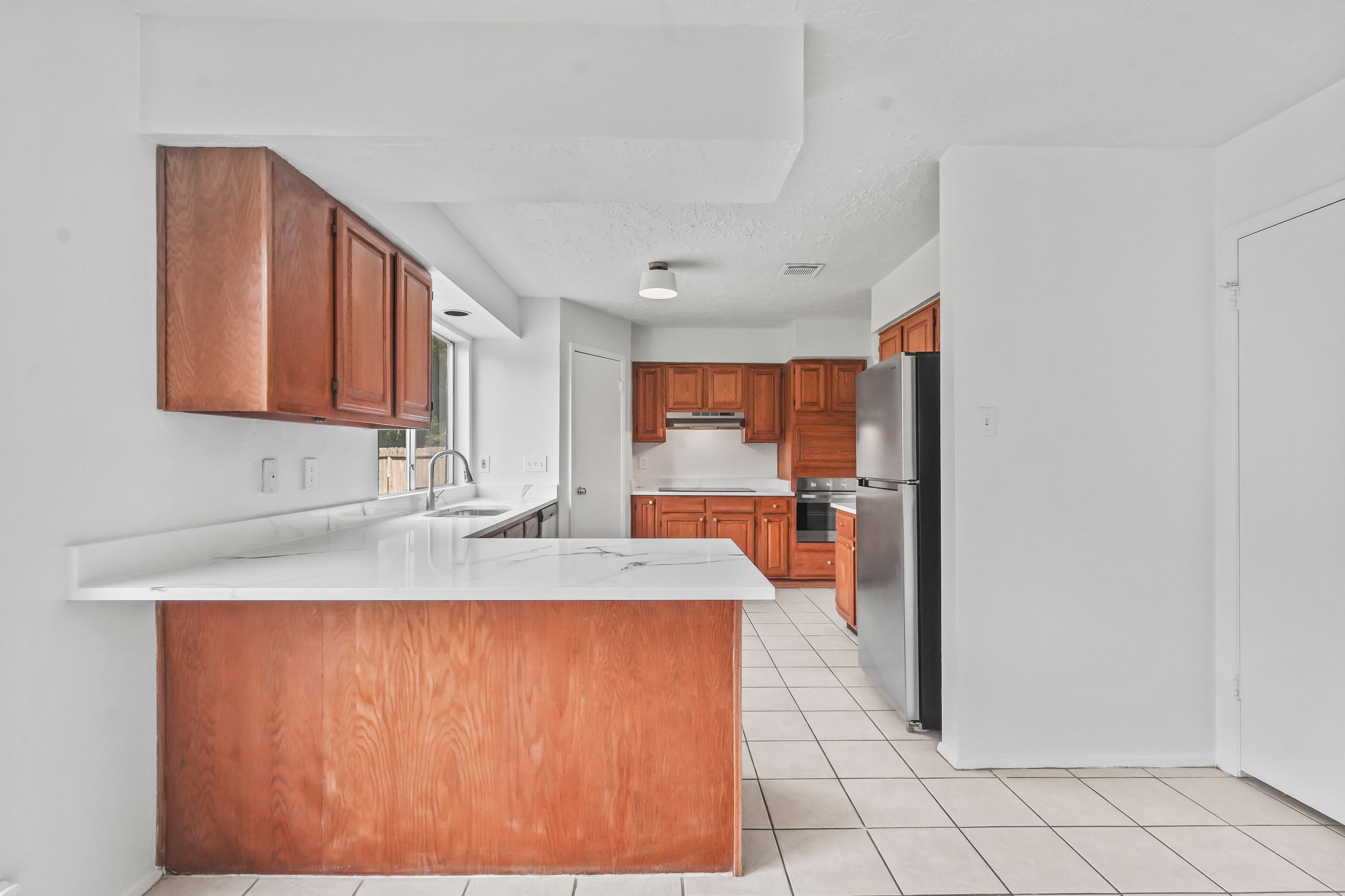 Spacious kitchen with wood cabinets, white countertops, stainless appliances, and light tile flooring in an open layout.