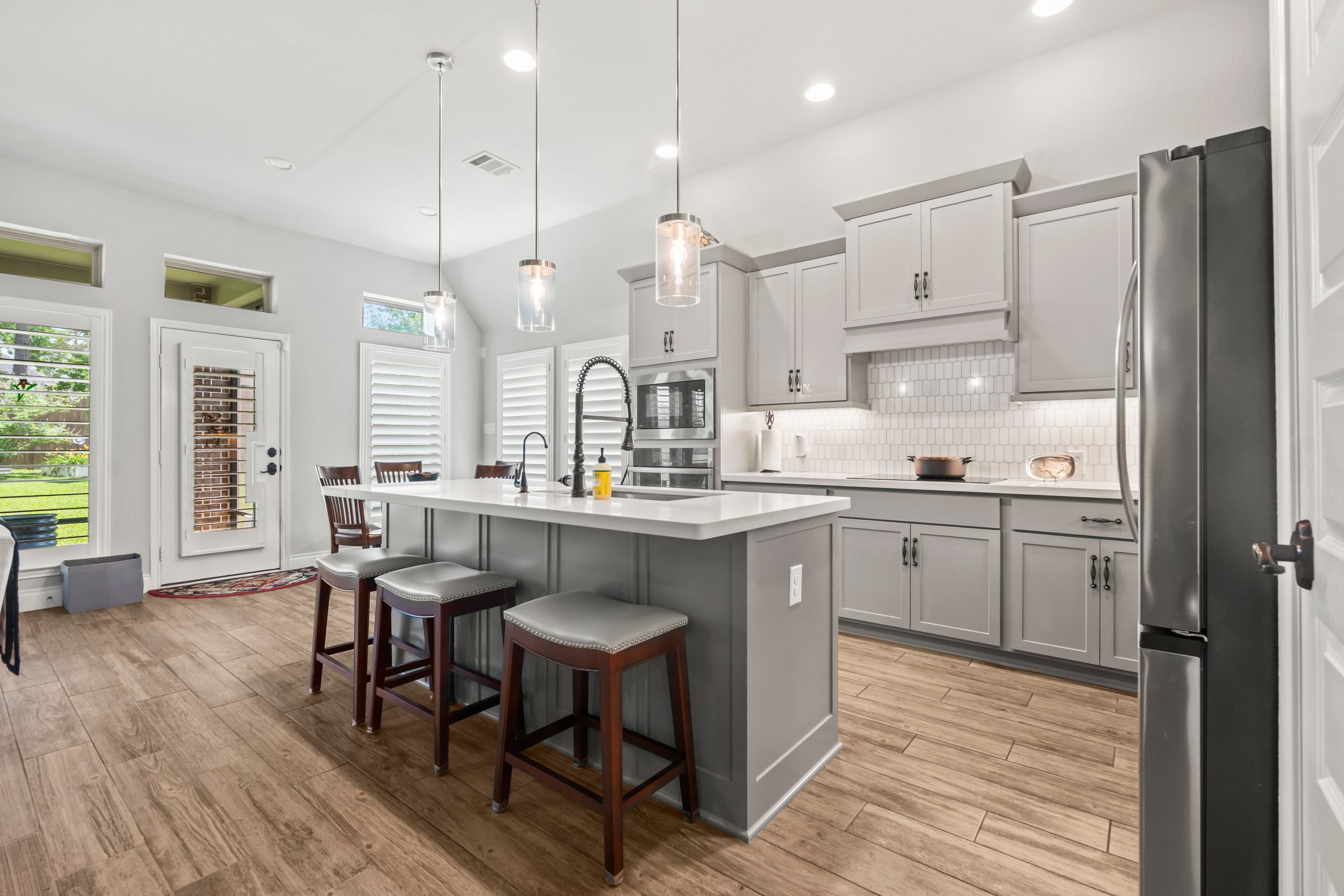 Modern kitchen with gray cabinets, island with seating, pendant lights, and stainless appliances.