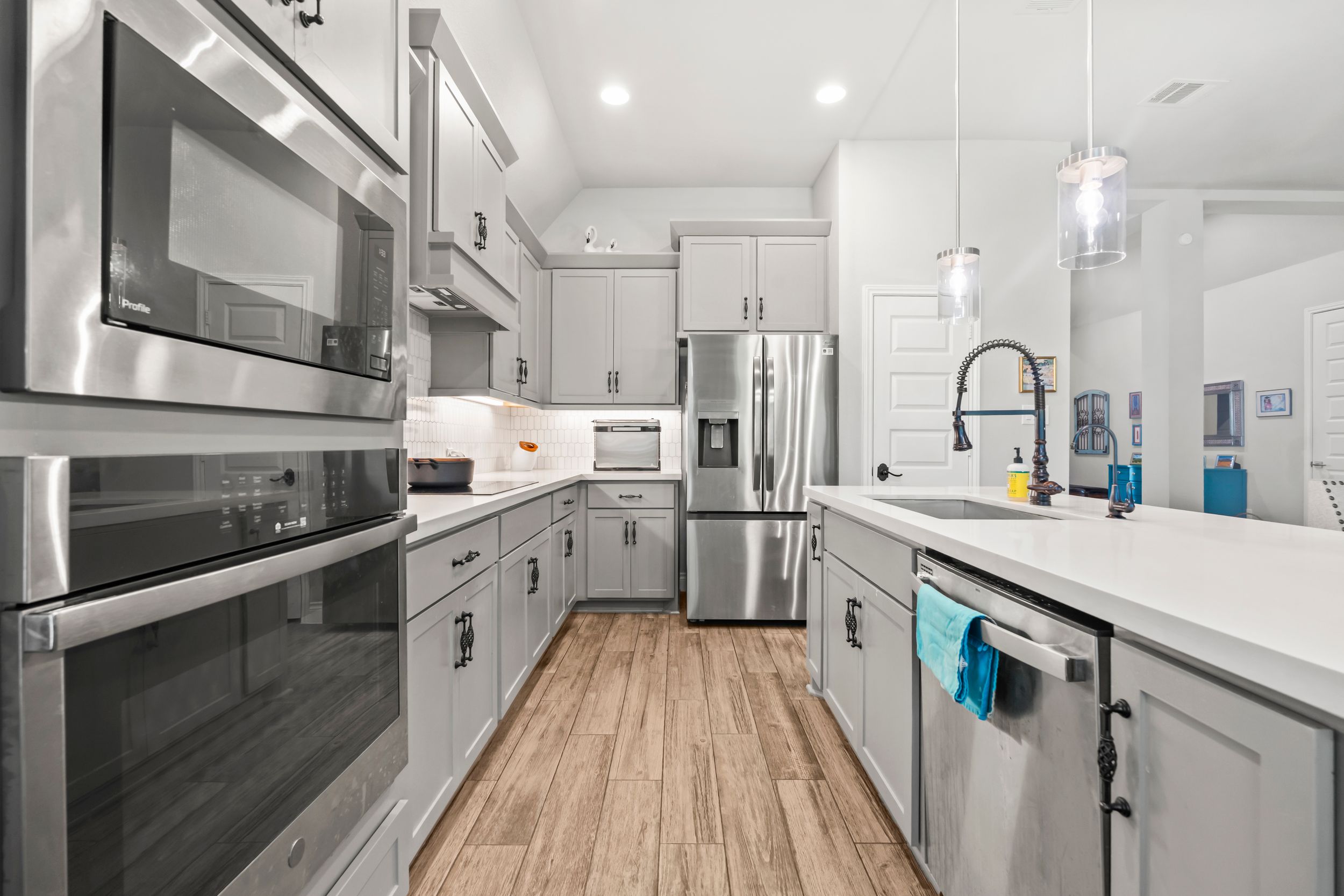 Modern kitchen with gray cabinets, stainless steel appliances, white countertops, and light wood flooring.